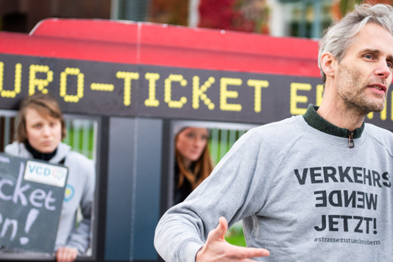 Personen bei einer Demonstration. Ein Mann trägt einen Pullover mit der Aufschrift "Vekehrs-Wende jetzt!"