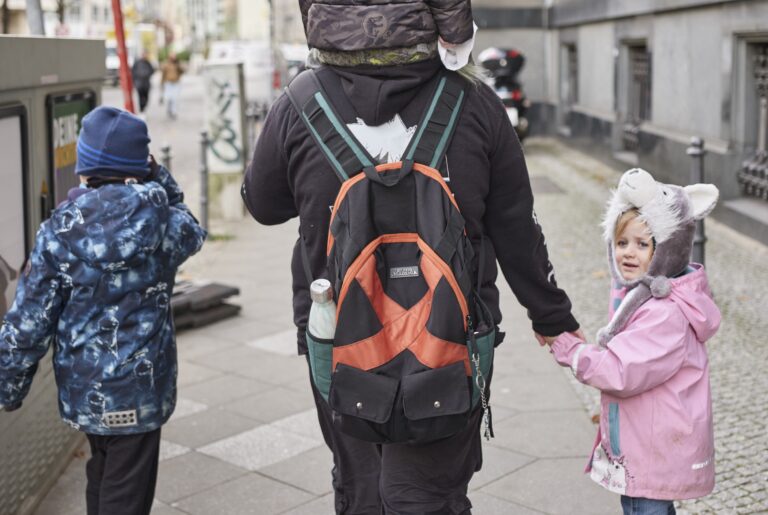 Ein Vater spaziert mit seinen drei Kindern über eine Innenstadtstraße.