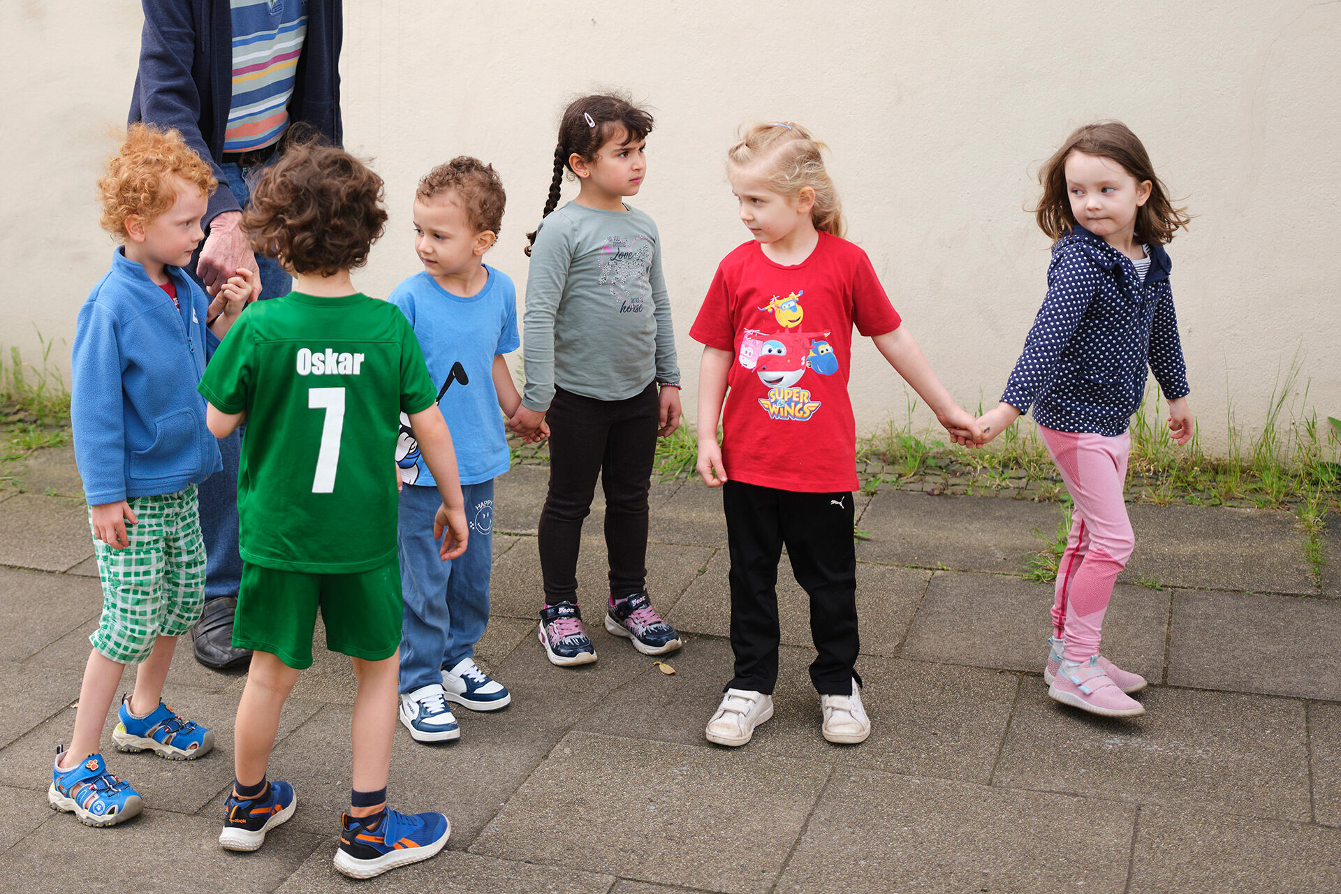 Sechs Kinder - Jungen und Mädchen - halten sich an den Händen und laufen auf einem Gehweg.