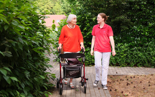 Pflegerin im roten Shirt mit AWO-Logo und Seniorin mit Rollator