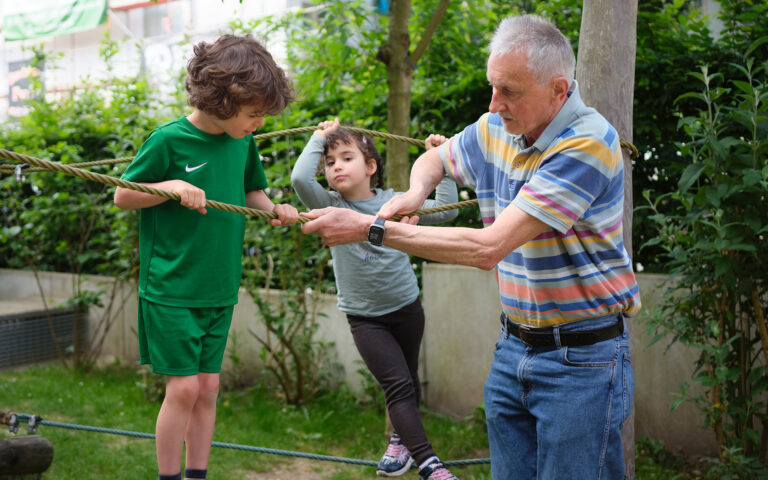 Schluss mit Sozialabbau - her mit der sozialen Garantie! Ein Senior hilft zwei Kindern beim Klettern.