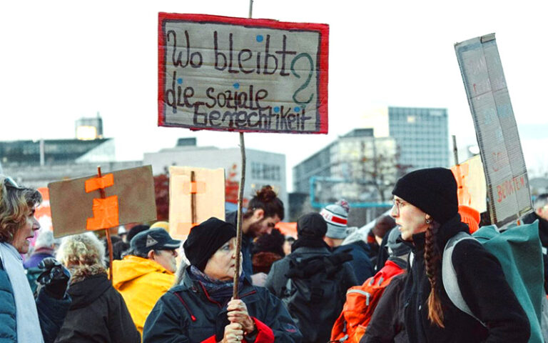 Personen auf Demo mit Schild "Wo bleibt die soziale Gerechtigkeit?"