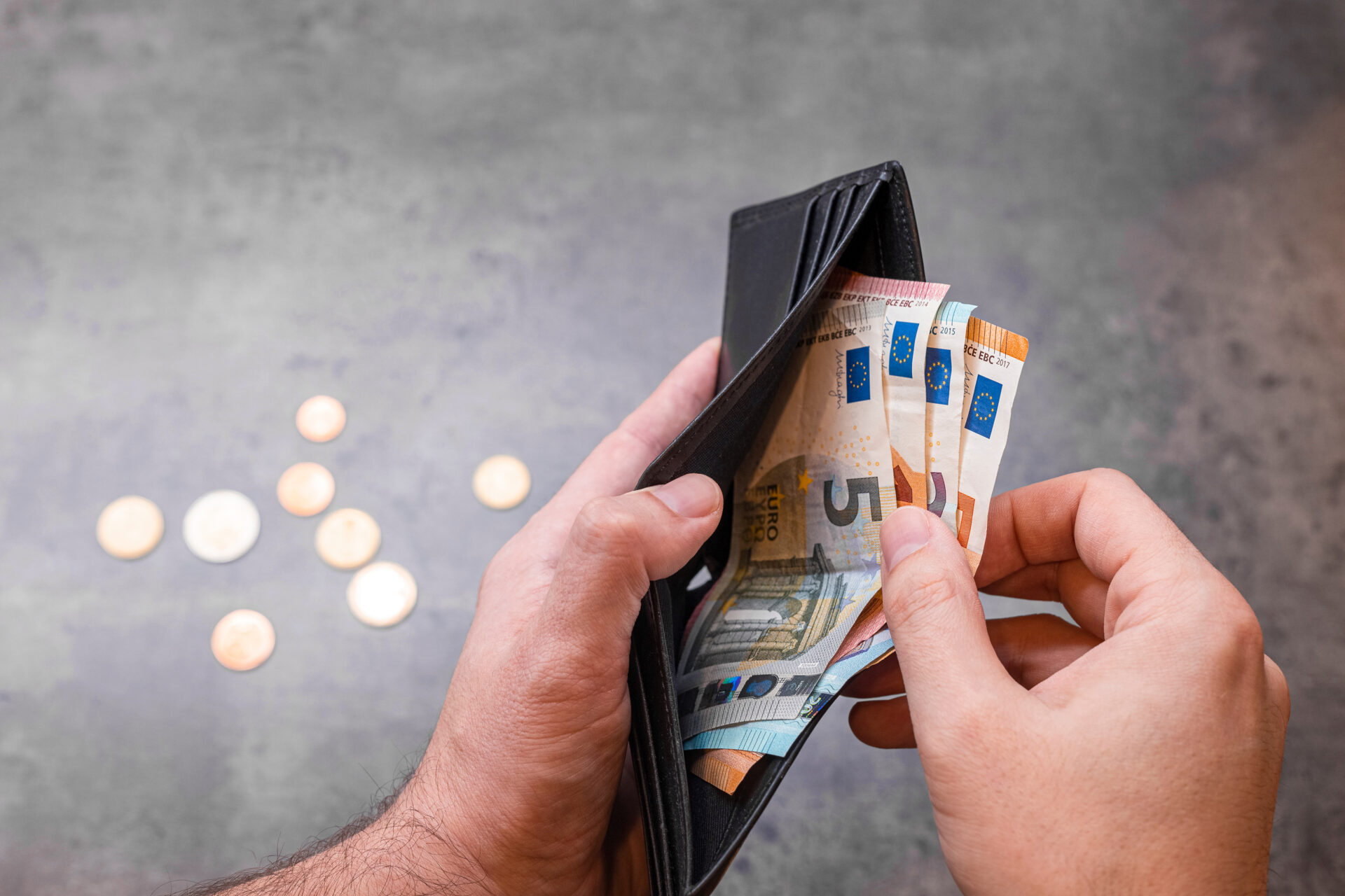 Zwei Hände, die ein Portemonnaie mit einigen Euro-Scheinen halten, daneben auf dem Tisch liegen einige Münzen