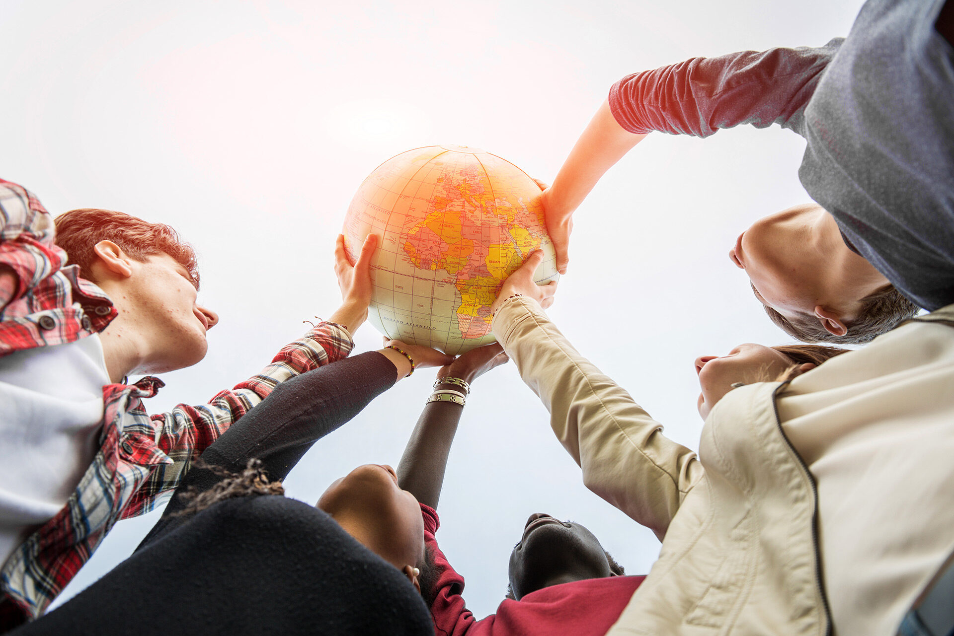 Fünf Teenager verschiedener Kulturen halten einen Globus in die Höhe.
