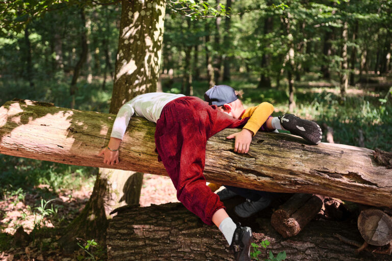 Zwei Kinder klettern im Wald über einen Baumstamm