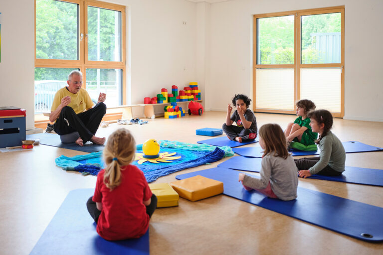 Gruppe von Kindern auf Yogamatten in einem hellen Raum mit großen Fenstern