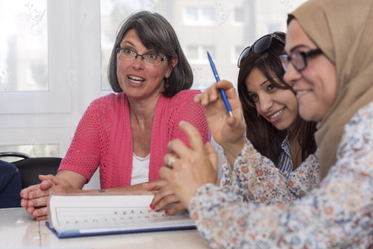 Drei Frauen in einem Kurs sitzen lachend am Tisch.