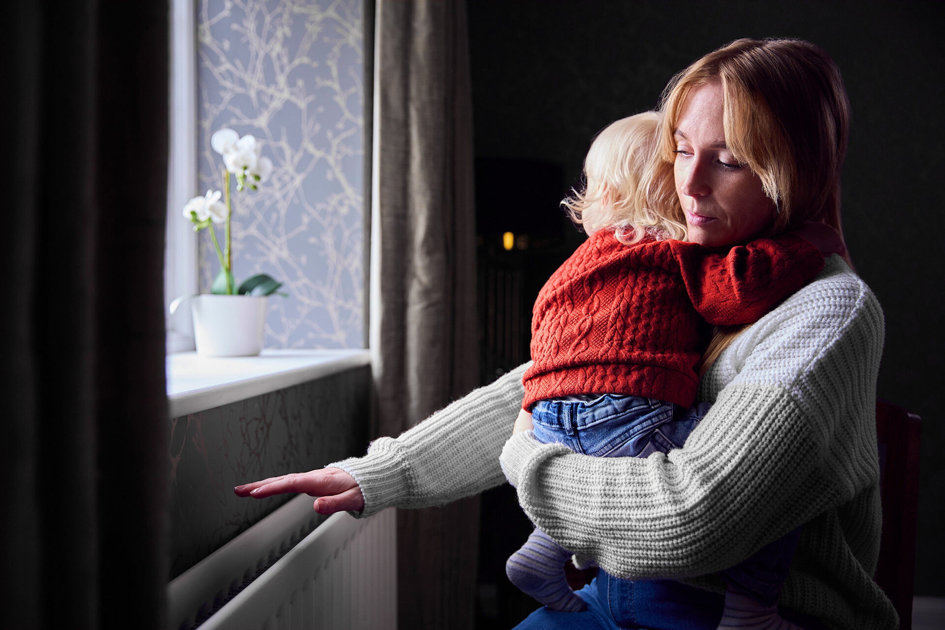 Eine Frau mit Kind auf dem Arm hält ihre Hand prüfend über die Heizung.
