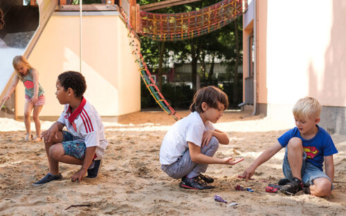 Vier Kinder spielen auf einem Spielplatz im Sand.
