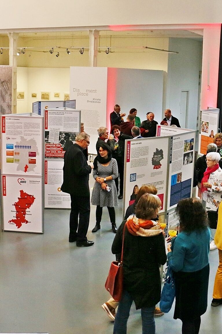 Bei der Ausstellung „Macherinnen. Helferinnen. Frauen und die AWO Schwaben“ schauen sich viele Personen die Informationsschilder und Tafeln an und unterhalten sich.