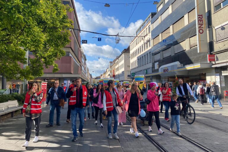 Bei einer Demonstration laufen viele Leute mit Schildern, roten Festen und Pfeifen durch die Straße.