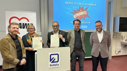 Fünf Personen stehen in einem Klassenraum und lächeln in die Kamera.