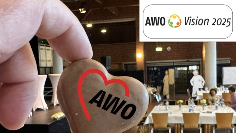 Nahaufnahme einer Hand, die ein Lebkuchenherz mit AWO Logo hält. Oben rechts steht "AWO Vision 2025".