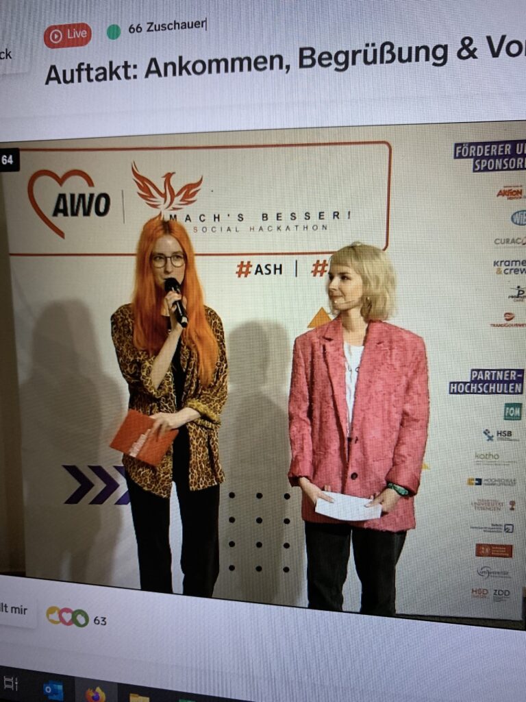 Aufnahme eines Laptop-Screens auf dem ein Live-Feed läuft. Dort sind zwei junge Frauen mit Mikrofonen vor AWO-Rollups zu sehen.