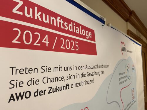 Schräge Nachaufnahme eines Plakat auf dem steht "Zukunftsdialog 2024/2025 - Treten Sie mit uns in den Austausch und nutzen Sie die Chance, sich in die Gestaltung der AWO der Zukunft einzubringen!"
