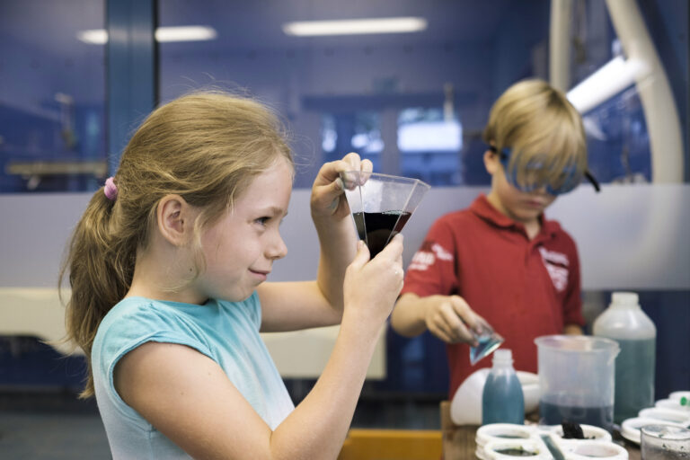 Zwei Kinder stehen in einem Labor und experimentieren mit flüssigen Substanzen.
