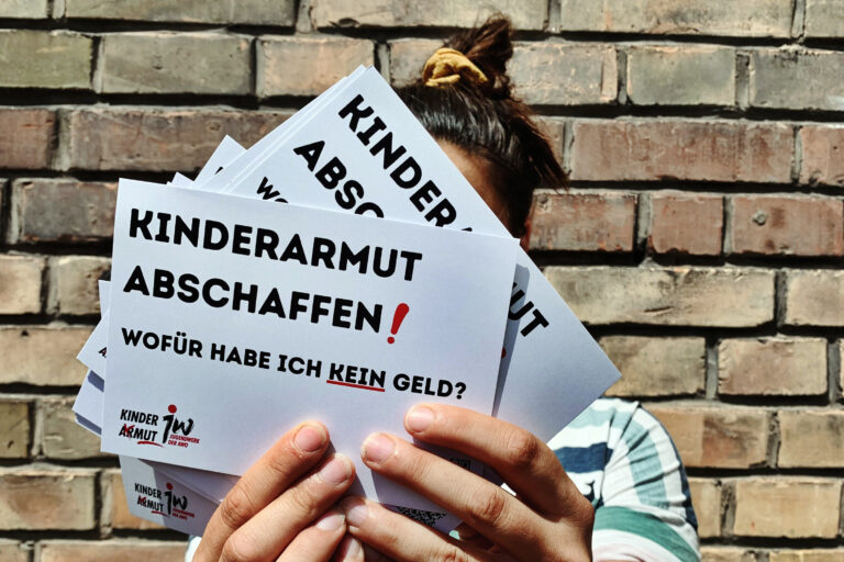 Eine Person hält einige Postkarten mit Jugendwerk-Logo, auf der vordersten steht "Kinderarmut abschaffen".
